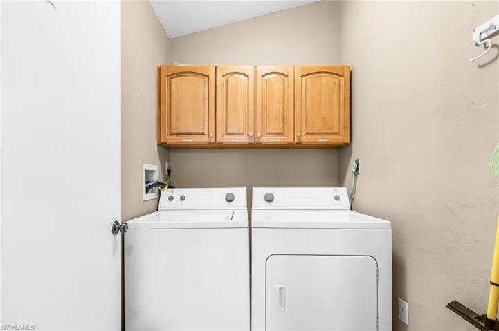 Laundry area featuring cabinet space, washer and clothes dryer, a textured wall, and vaulted ceiling