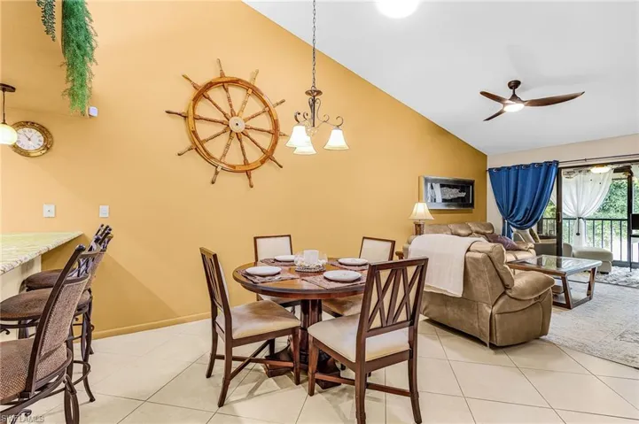 Dining area with a ceiling fan, light tile patterned floors, vaulted ceiling, and a chandelier