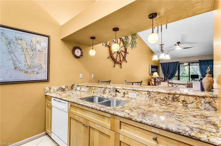 Kitchen featuring light stone countertops, dishwasher, hanging light fixtures, vaulted ceiling, and light tile patterned floors
