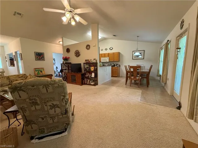 Living room featuring vaulted ceiling, light carpet, ceiling fan, and light tile patterned floors