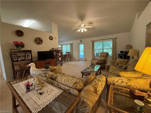 Living room with lofted ceiling, carpet flooring, and a ceiling fan