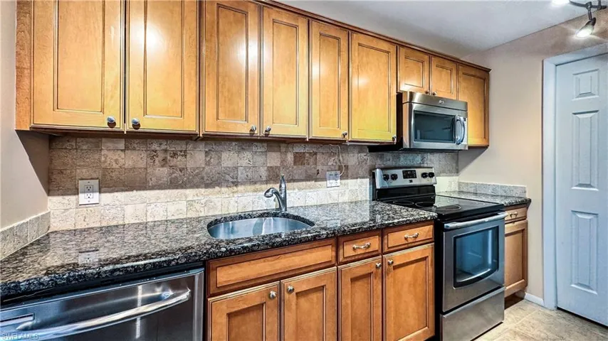 Kitchen featuring dark stone countertops, light tile patterned floors, stainless steel appliances, decorative backsplash, and sink