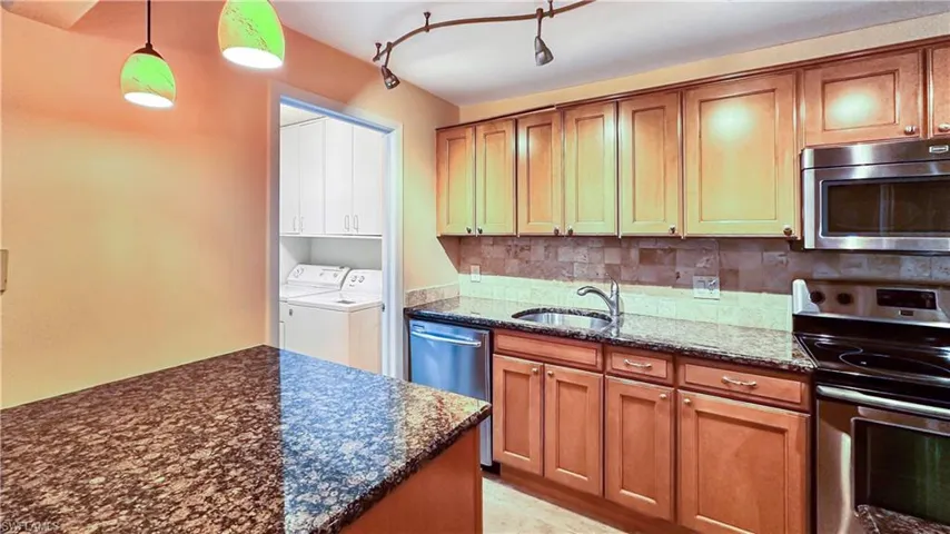 Kitchen with appliances with stainless steel finishes, washing machine and dryer, track lighting, sink, and hanging light fixtures