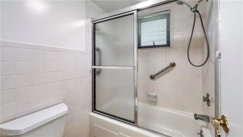Bathroom with tile walls, enclosed tub / shower combo, and toilet