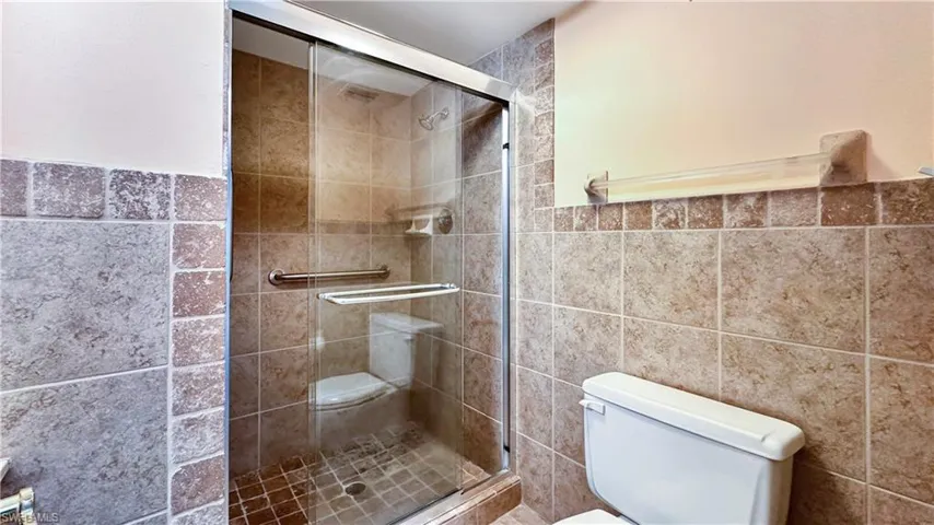 Bathroom featuring an enclosed shower, tile walls, and toilet