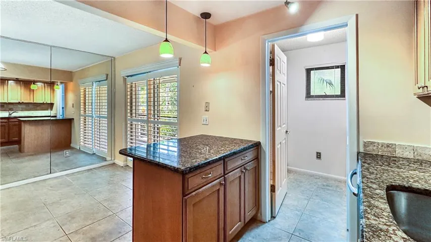 Kitchen featuring light tile patterned flooring, decorative backsplash, hanging light fixtures, and dark stone countertops