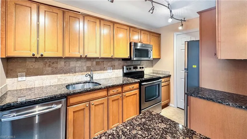 Kitchen featuring dark stone counters, light tile patterned flooring, stainless steel appliances, sink, and track lighting