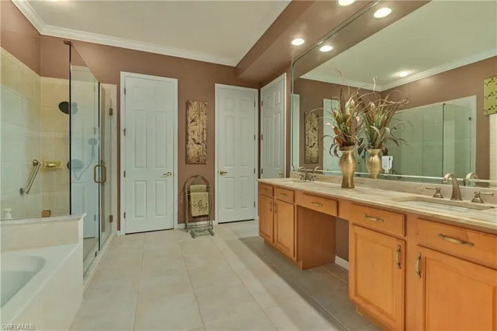Full bathroom featuring ornamental molding, double vanity, a shower stall, a garden tub, and light tile patterned floors