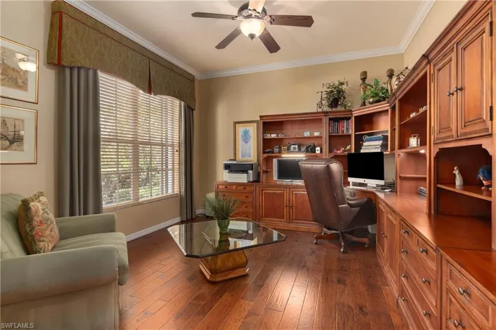 Office space featuring ornamental molding, built in desk, ceiling fan, and dark wood-type flooring