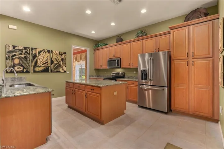 Kitchen with appliances with stainless steel finishes, a kitchen island, light stone countertops, recessed lighting, and brown cabinetry