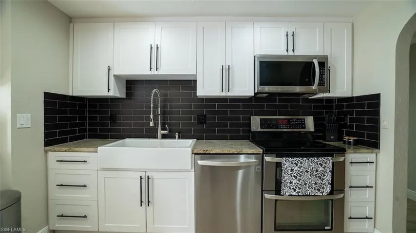 Kitchen with stainless steel appliances, white cabinets, light stone counters, arched walkways, and tasteful backsplash