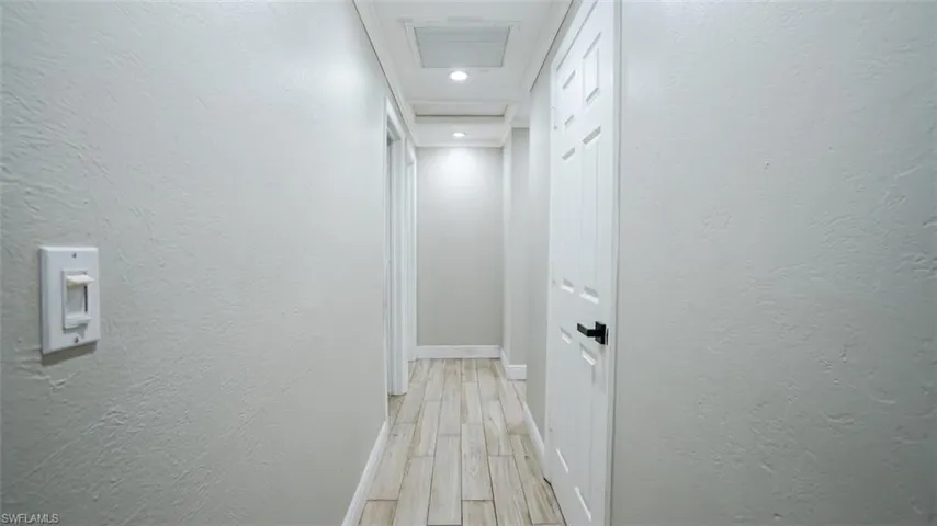 Hall featuring a textured wall, light wood finished floors, and recessed lighting