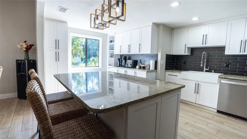 Kitchen with light stone counters, dishwasher, light wood-style flooring, tasteful backsplash, and two tone cabinets