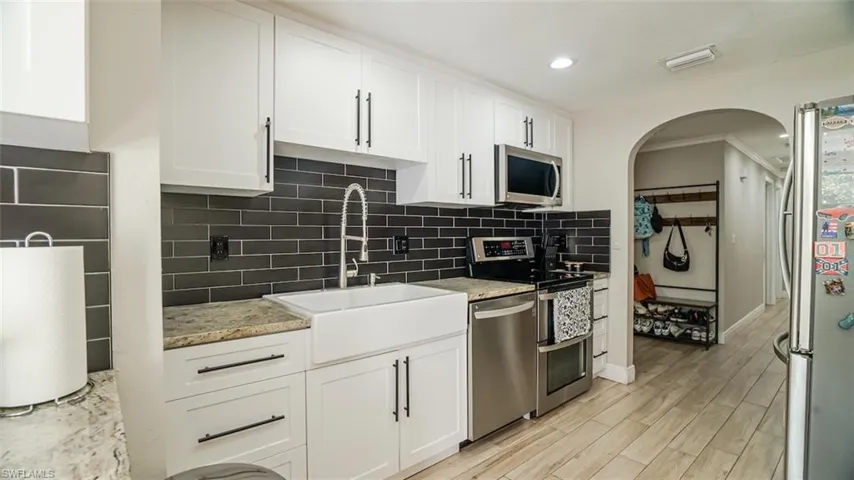Kitchen with stainless steel appliances, white cabinets, arched walkways, recessed lighting, and crown molding