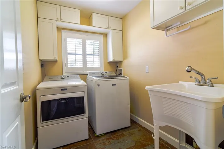 Laundry area with plantation shutters, sink, cabinets, washer and clothes dryer.
