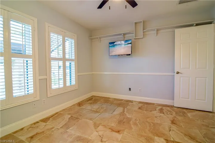 Guest bedroom #3 with wall mounted television, ceiling fan, & decorative shelving.