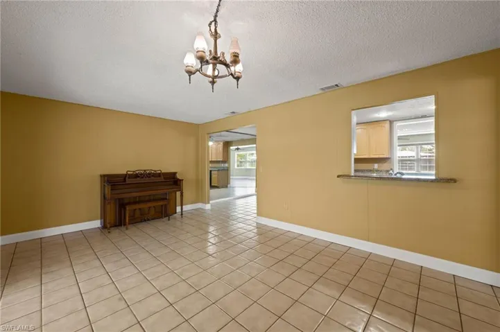 Tiled empty room featuring a chandelier and a textured ceiling