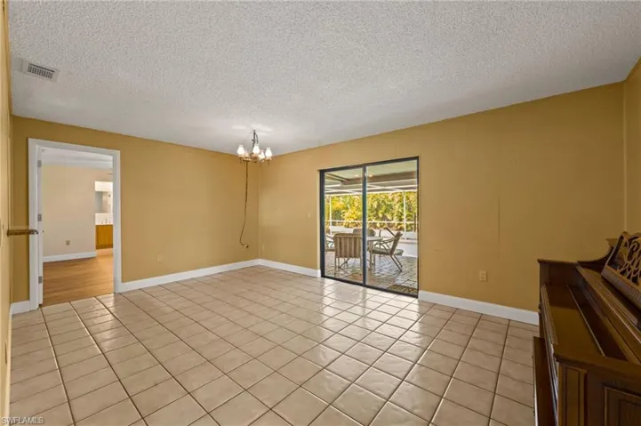 Empty room with light tile patterned floors, a textured ceiling, and a notable chandelier