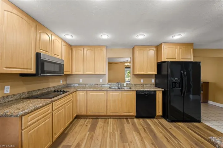 Kitchen with light brown cabinetry, dark stone counters, sink, black appliances, and light hardwood / wood-style flooring