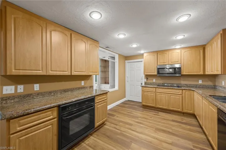 Kitchen with a textured ceiling, light hardwood / wood-style flooring, dark stone countertops, and black appliances