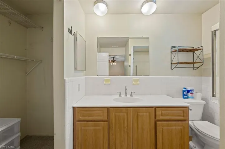 Bathroom featuring ceiling fan, toilet, tile walls, and vanity