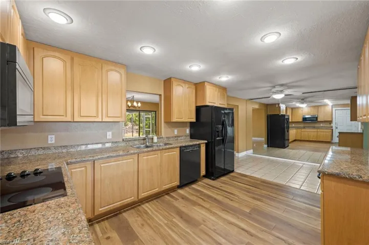 Kitchen with sink, light hardwood / wood-style flooring, a textured ceiling, light brown cabinetry, and black appliances