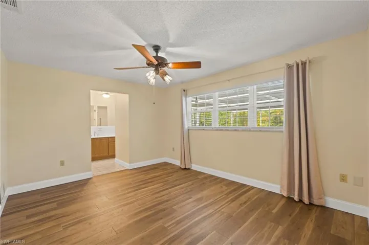 Unfurnished bedroom featuring hardwood / wood-style floors, ceiling fan, a textured ceiling, and ensuite bath
