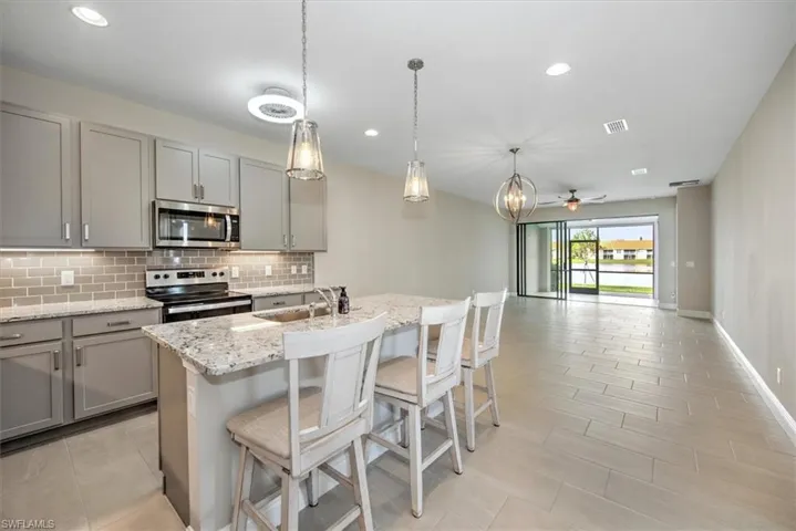 Kitchen with ceiling fan, appliances with stainless steel finishes, gray cabinetry, and a center island with sink