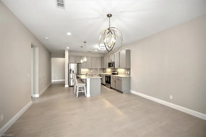 Kitchen with a center island with sink, gray cabinets, stainless steel appliances, decorative light fixtures, and a kitchen breakfast bar