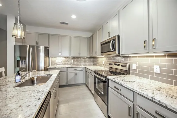 Kitchen with stainless steel appliances, gray cabinetry, hanging light fixtures, light stone counters, and sink