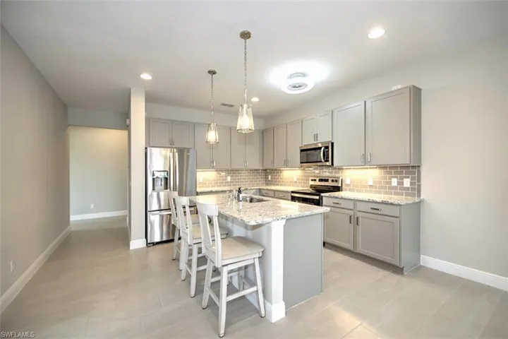 Kitchen featuring appliances with stainless steel finishes, a kitchen bar, an island with sink, sink, and light stone counters