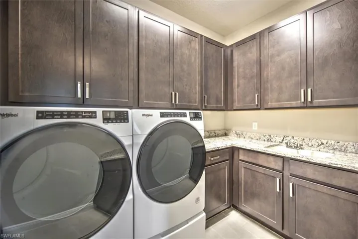 Washroom with light tile patterned floors, sink, washing machine and clothes dryer, and cabinets
