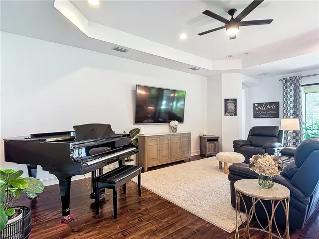 Living room featuring a raised ceiling, ceiling fan, and dark hardwood / wood-style floors