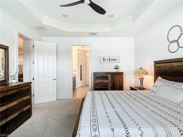 Carpeted bedroom with ensuite bath, ceiling fan, and a tray ceiling