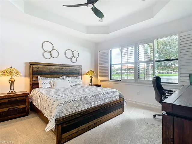 Bedroom with light carpet, a raised ceiling, multiple windows, and ceiling fan