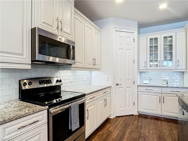 Kitchen with decorative backsplash, appliances with stainless steel finishes, dark hardwood / wood-style floors, and white cabinets