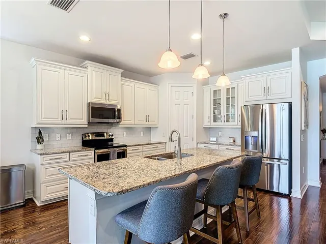 Kitchen featuring tasteful backsplash, dark wood-type flooring, light stone countertops, appliances with stainless steel finishes, and sink