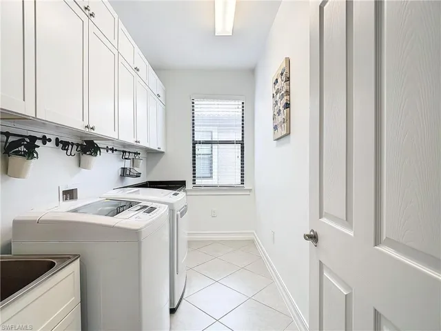 Laundry room with light tile patterned floors, washing machine and clothes dryer, sink, and cabinets