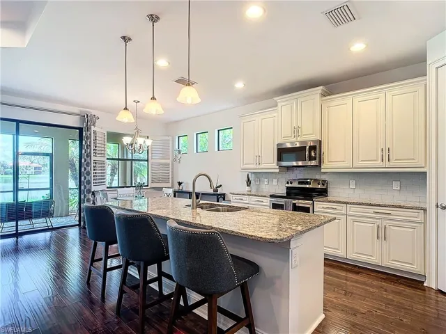 Kitchen with decorative light fixtures, stainless steel appliances, dark hardwood / wood-style flooring, decorative backsplash, and light stone countertops
