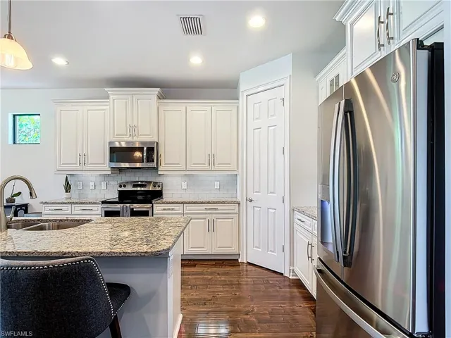 Kitchen featuring hanging light fixtures, sink, light stone countertops, dark hardwood / wood-style floors, and appliances with stainless steel finishes