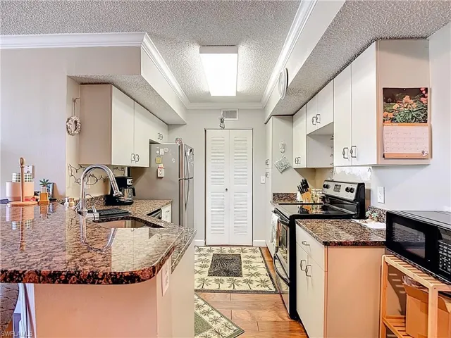 Kitchen featuring electric range, crown molding, white cabinetry, a peninsula, and dark stone countertops