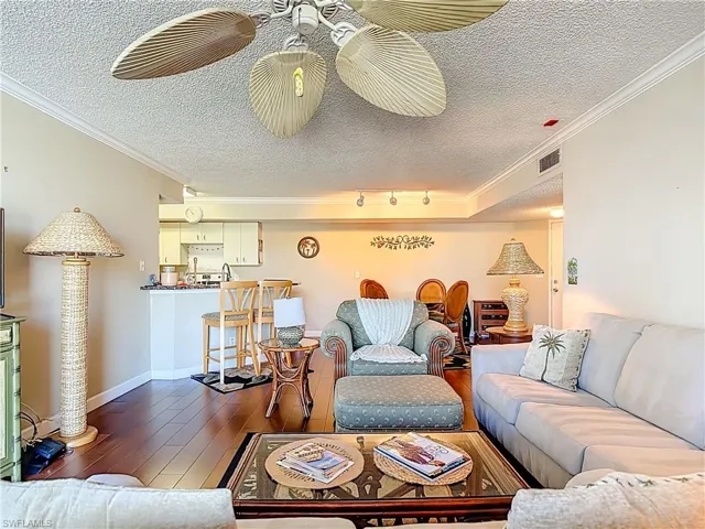 Living room with a textured ceiling, ornamental molding, and dark wood-style flooring