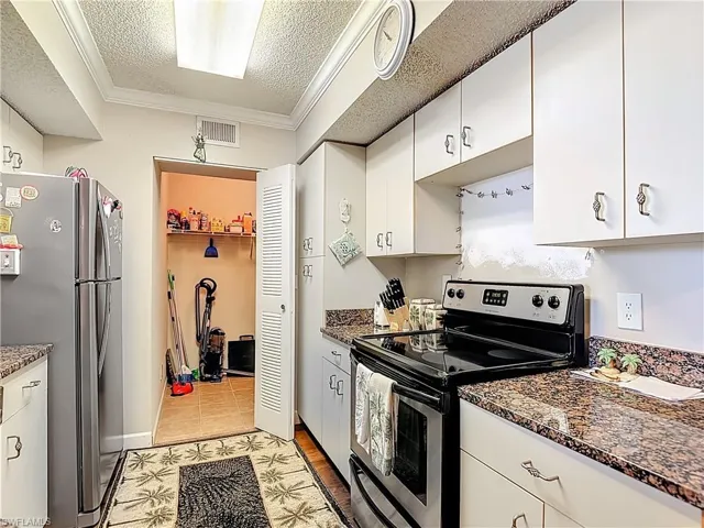 Kitchen with stainless steel appliances, white cabinets, a textured ceiling, crown molding, and dark stone countertops