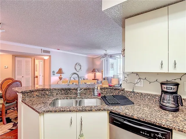 Kitchen featuring dark stone counters, dishwasher, a peninsula, a textured ceiling, and crown molding