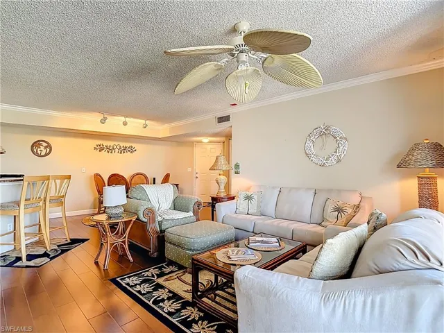 Living area with crown molding, a textured ceiling, wood finished floors, and a ceiling fan