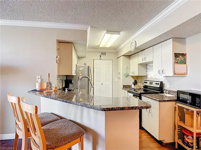 Kitchen with ornamental molding, white cabinetry, a peninsula, a breakfast bar, and stainless steel appliances