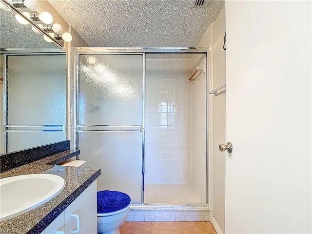 Full bath featuring vanity, a stall shower, a textured ceiling, and light tile patterned floors