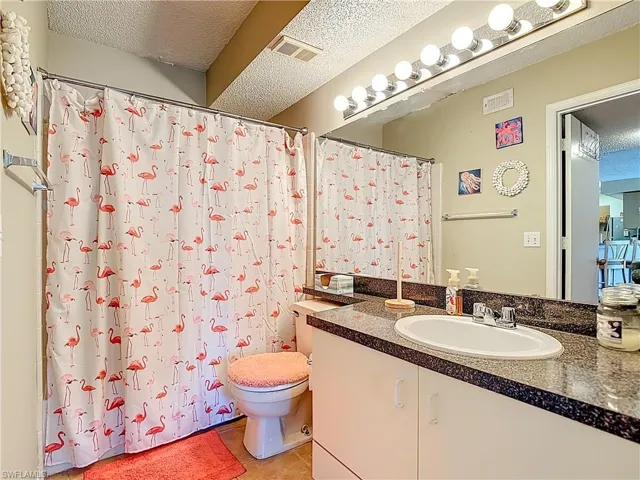 Full bath with a textured ceiling, vanity, curtained shower, and light tile patterned flooring