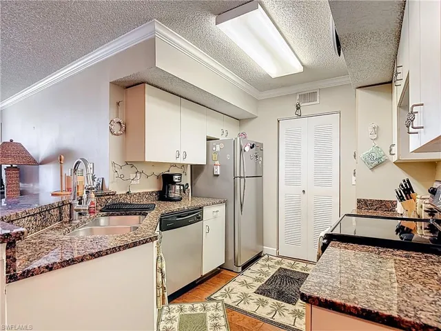 Kitchen featuring crown molding, white cabinetry, stainless steel appliances, dark stone counters, and a textured ceiling