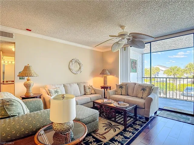 Living room with a textured ceiling, hardwood / wood-style floors, a ceiling fan, and crown molding